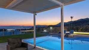 Ein überdachter Außenpool mit Liegestühlen und einem Tisch, umgeben von einer Steinmauer und Blick auf den Sonnenuntergang über den Hügeln.