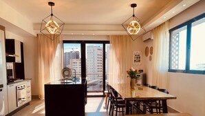 Una cocina moderna con una isla central, un comedor con mesa y sillas de madera, y vistas a la ciudad a través de amplios ventanales.