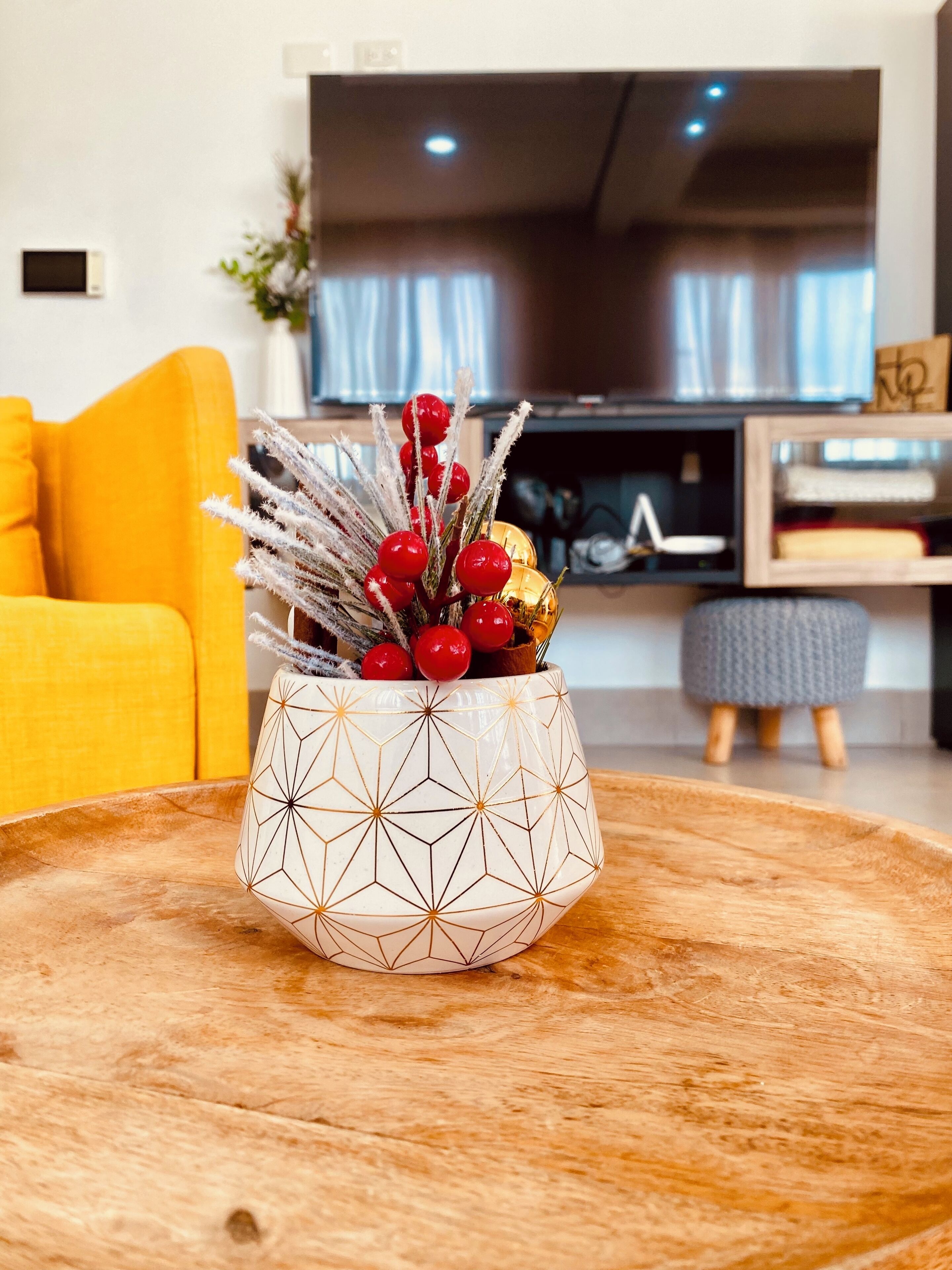 Ein modernes Wohnzimmer mit einer geometrisch gemusterten Vase auf einem Holztisch, einem gelben Sofa und einem Flachbildfernseher im Hintergrund.