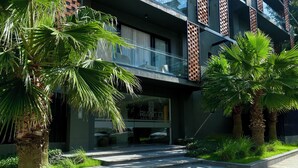 Un edificio moderno con fachada de vidrio, un muro de acento de ladrillo y un jardín bien cuidado con palmeras.
