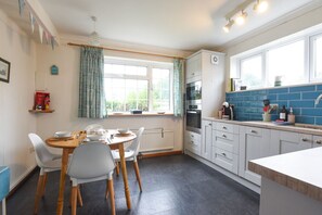 A kitchen with a dining table, chairs, a window with curtains, an oven, and a sink with blue tiles.