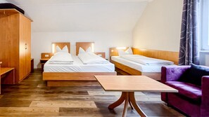 A hotel room with two beds, a wooden wardrobe, a small table, and a purple armchair.