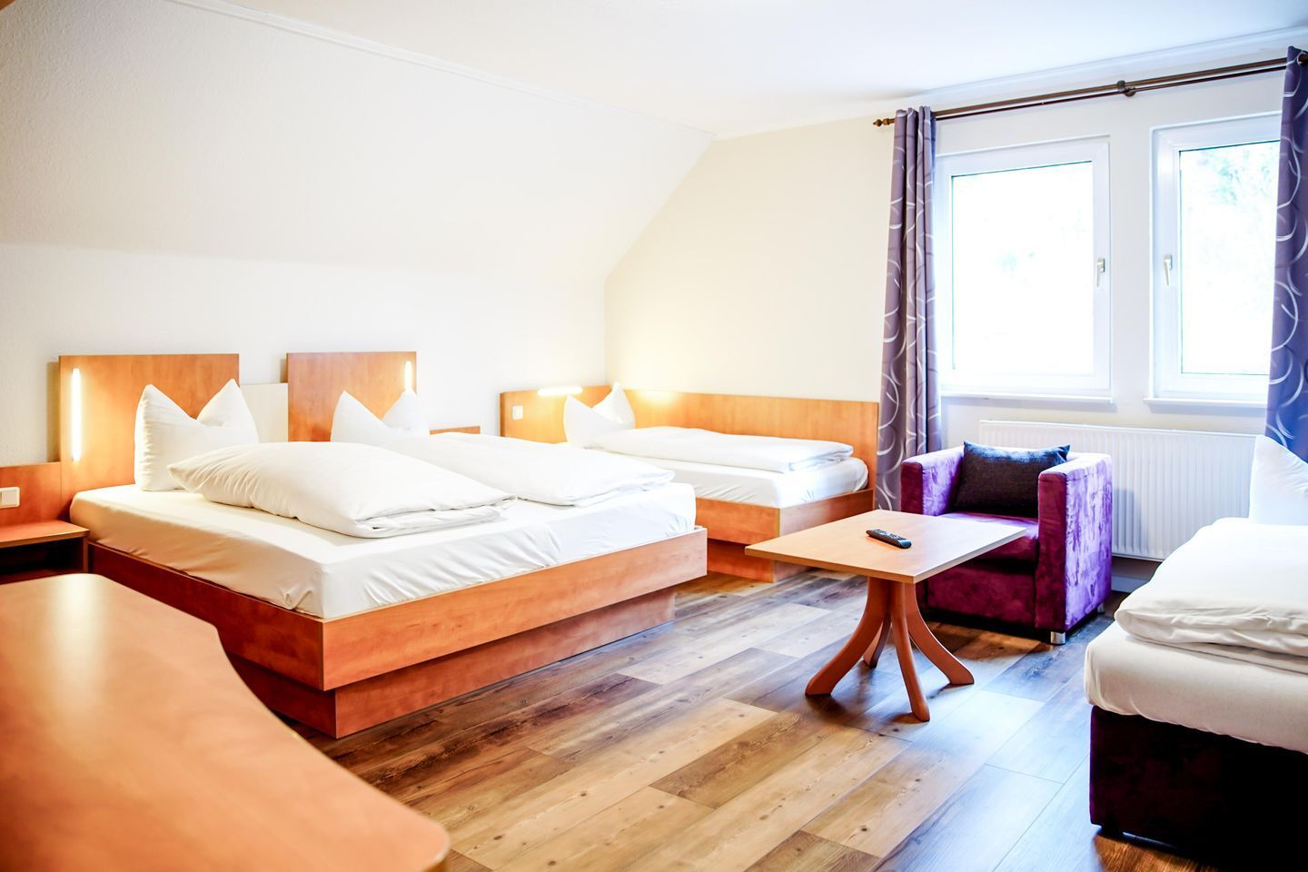 Una habitación de hotel con dos camas, un sofá, una mesita y una ventana con cortinas.
