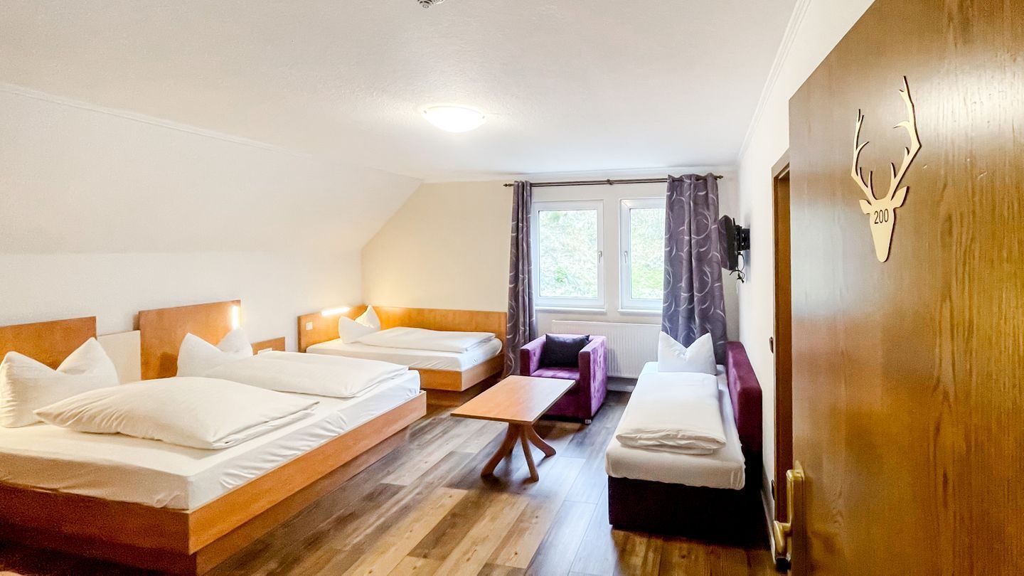 A room with two beds, a sofa, a small table, and a window with curtains.