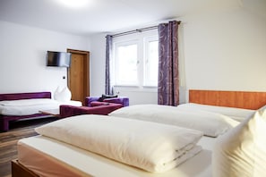 Una habitación de hotel con dos camas, un sofá, un televisor y una ventana con cortinas.