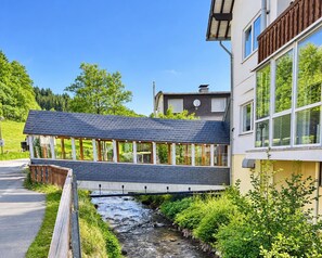 A modern building with a bridge over a stream, surrounded by greenery. - Comfortable and versatile room -perfect for relaxation, work and exchange (Winterberg)