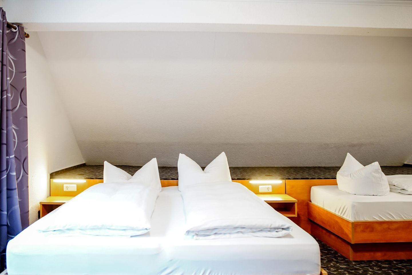A hotel room with two beds, each with white bedding and pillows, a headboard, and a nightstand with a lamp.