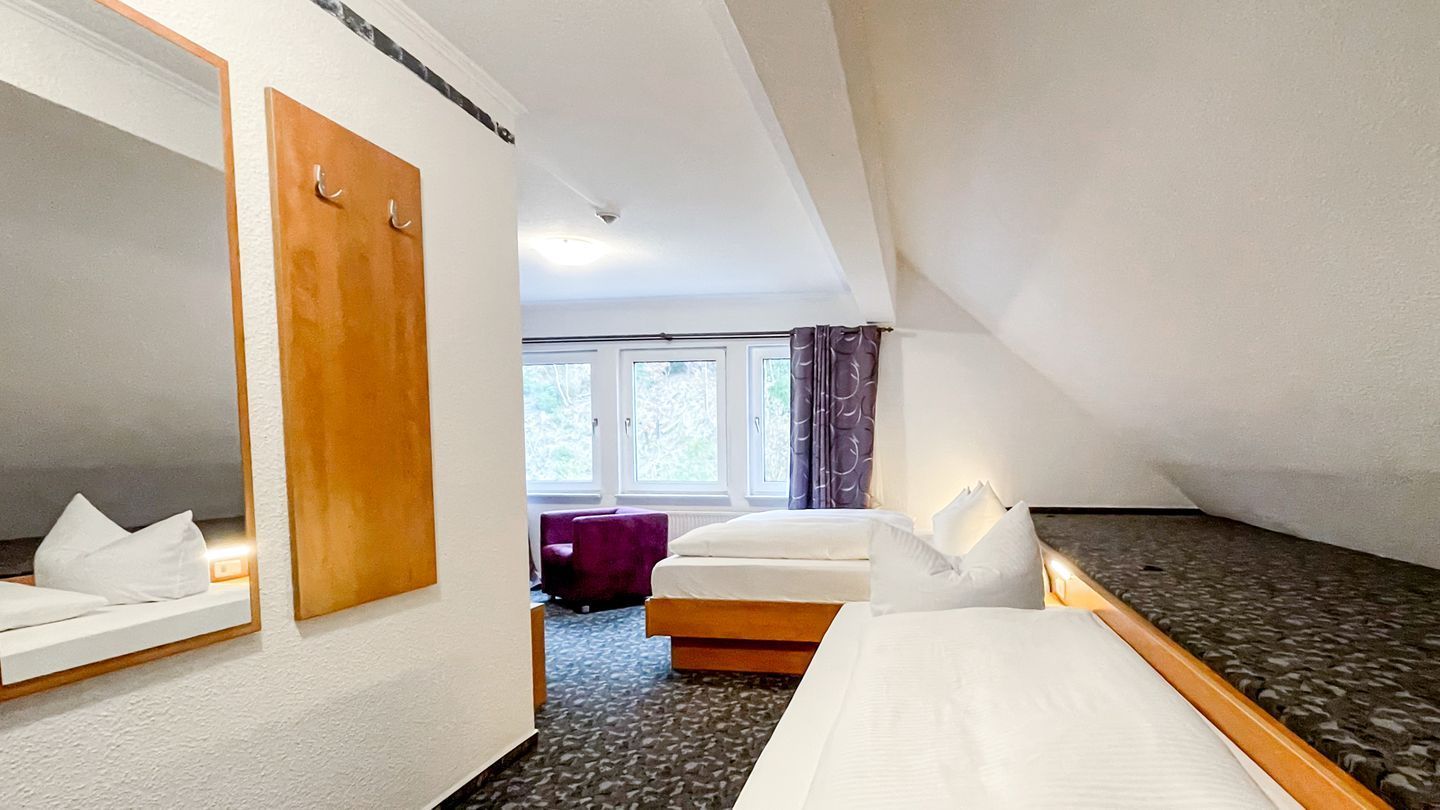 A hotel room with a bed, a mirror, a wooden door, a window, and a purple chair.