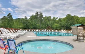 A swimming pool with lounge chairs and a hot tub, surrounded by trees.