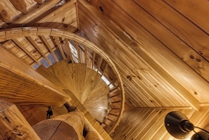 A spiral staircase in a wooden interior with a ceiling fan.