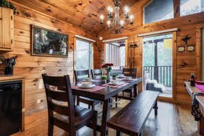 A wooden cabin interior with a dining table set for four, a chandelier, and a framed picture of bears on the wall.