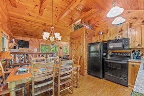 A wooden cabin interior with a dining area, kitchen, and a large window.