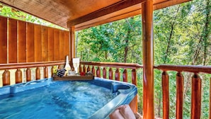Een hottub op een houten terras, met uitzicht op een bos.