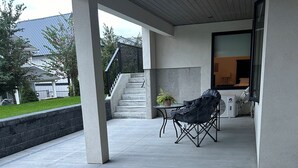 A covered outdoor area with a concrete floor, a table with a potted plant, and a folding chair. There is a staircase leading to a building with a glass door. - Luxury Suite situated on top of mountain in a prestigious location. (Abbotsford)