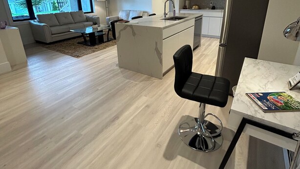 A modern kitchen with a central island, a dining area with a bar stool, and a living room with a sofa and a TV. - Luxury Suite situated on top of mountain in a prestigious location. (Abbotsford)