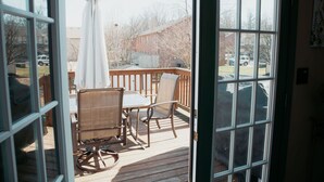 A deck with a table and chairs, a white umbrella, and a view of a house and cars in the background.