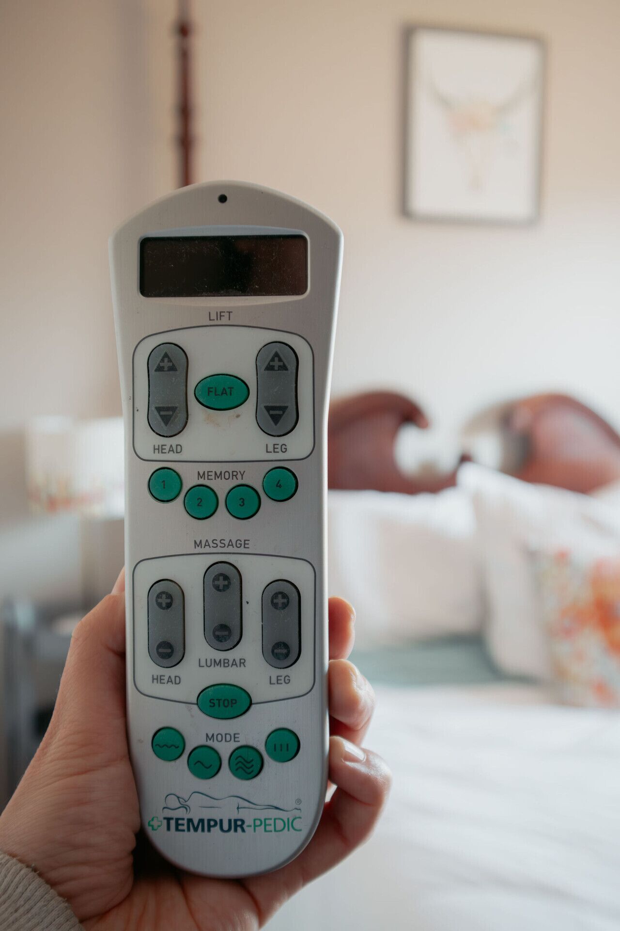 A person holding a TEMPUR-PEDIC massage chair remote control.