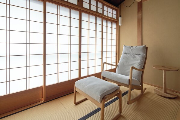 A traditional Japanese room with tatami flooring, a low wooden table, and a cushioned chair.