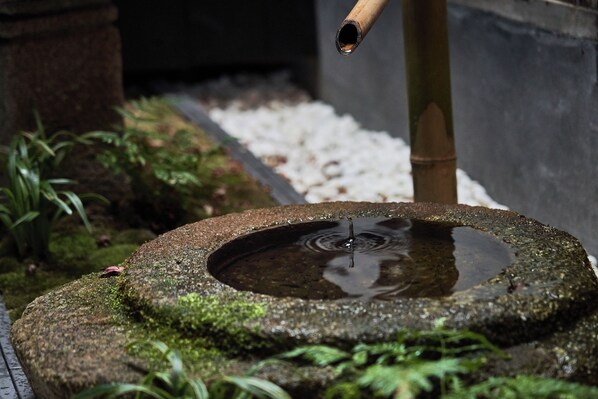 A stone water feature with a bamboo spout, surrounded by moss and small plants. - YADORU KYOTO HANARE Kagetsu No Yado (Kyoto)