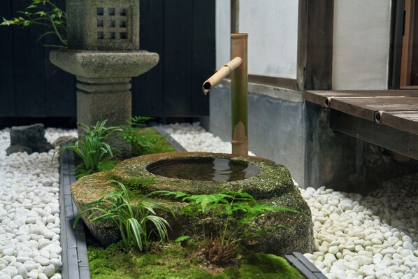 Una cuenca de piedra con agua, rodeada de guijarros blancos y plantas verdes.
