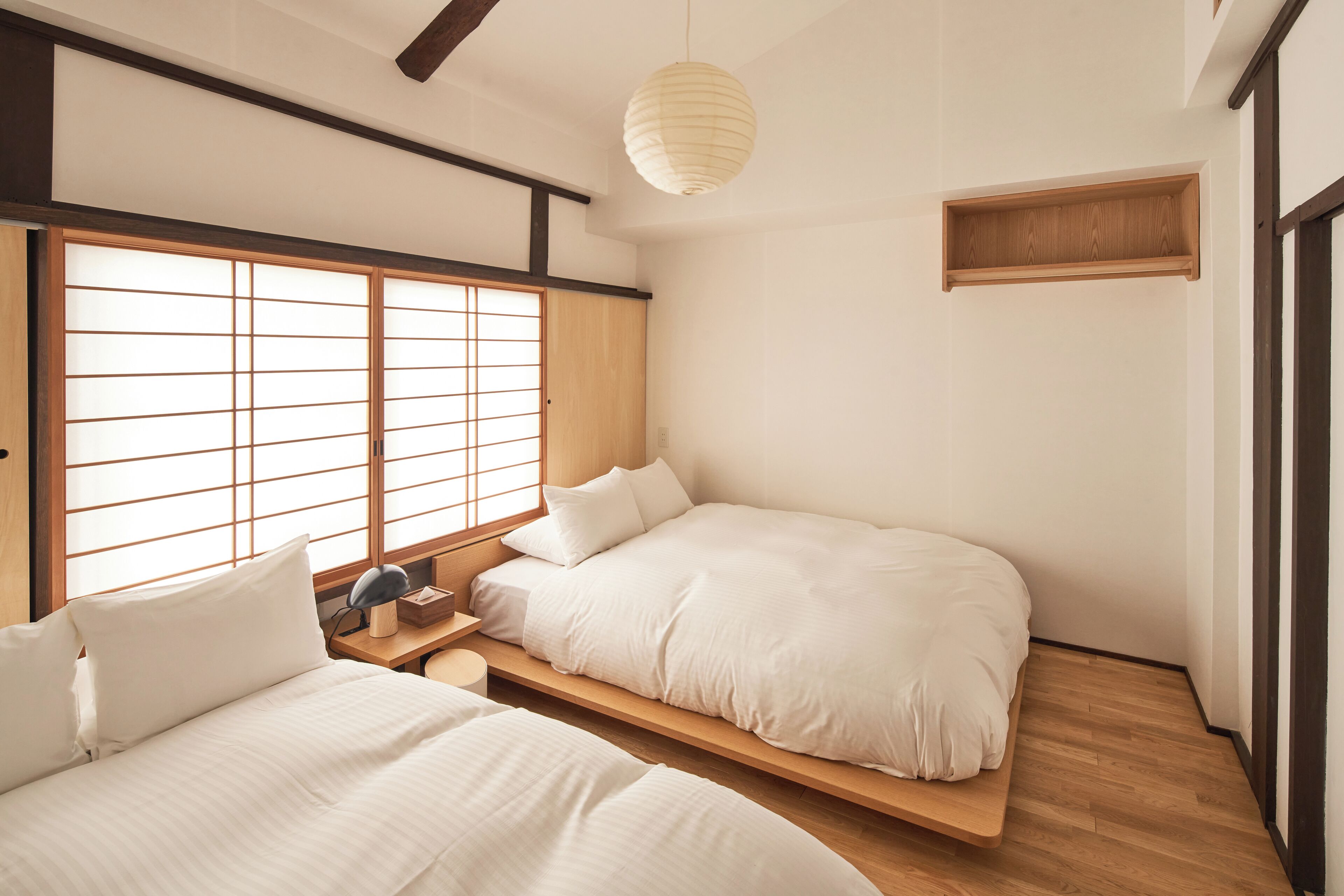 A traditional Japanese-style bedroom with two beds, a wooden shelf, and a paper lantern.
