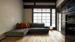 A modern living room with a grey sectional sofa, wooden flooring, a large window with traditional-style blinds, and a dark wooden cabinet. - YADORU KYOTO HANARE Shirotaki No Yado (Kyoto)