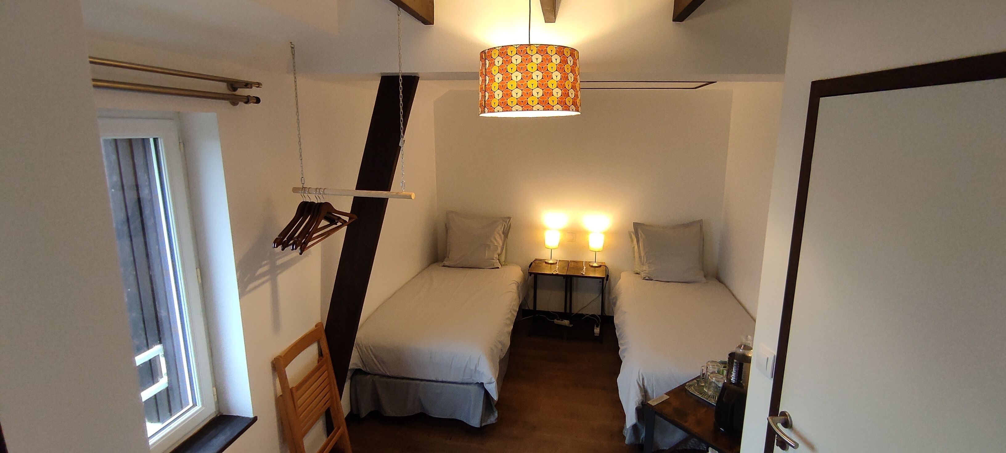 Un dormitorio con dos camas, un sillón colgante, una mesita de noche con lámparas y una ventana.