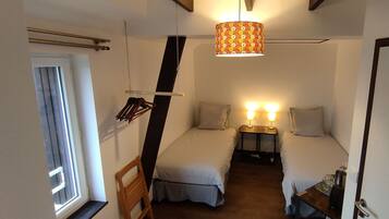 Un dormitorio con dos camas, un sillón colgante, una mesita de noche con lámparas y una ventana.