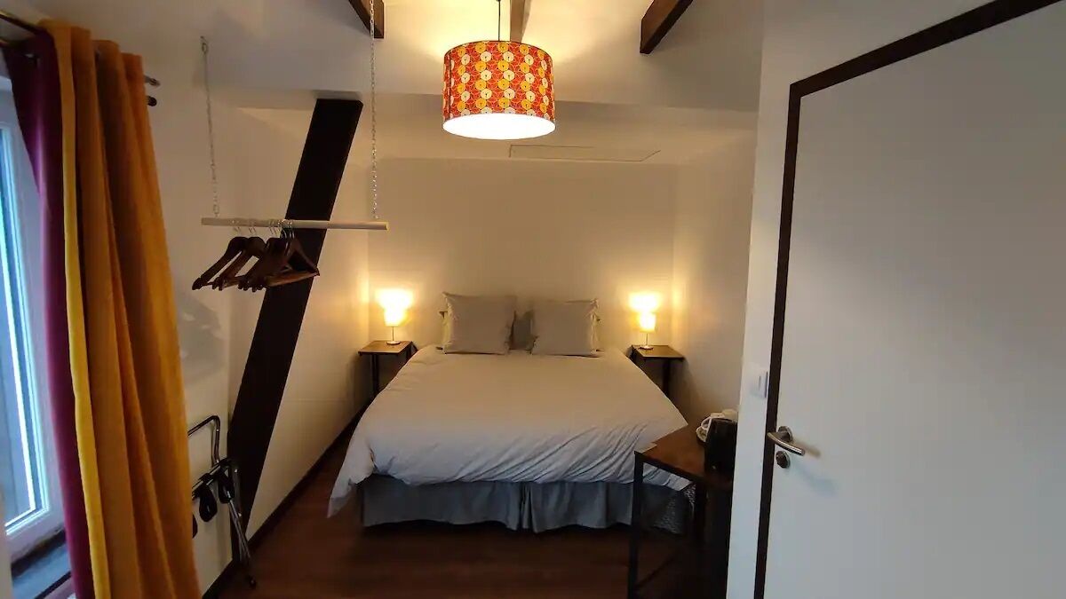 A bedroom with a bed, bedside lamps, a hanging lamp, and a door.