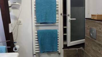A bathroom with a toilet, a sink, a towel rack with blue towels, a shower door, and a trash bin.