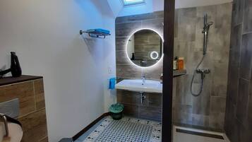 Een badkamer met dakraam, douche, wastafel en toilet.