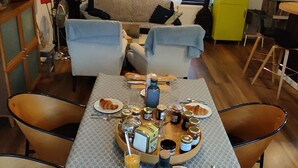 A dining area with a table set for breakfast, including croissants, fruits, and beverages. - Le petit moulin rouge (Beauvoir)