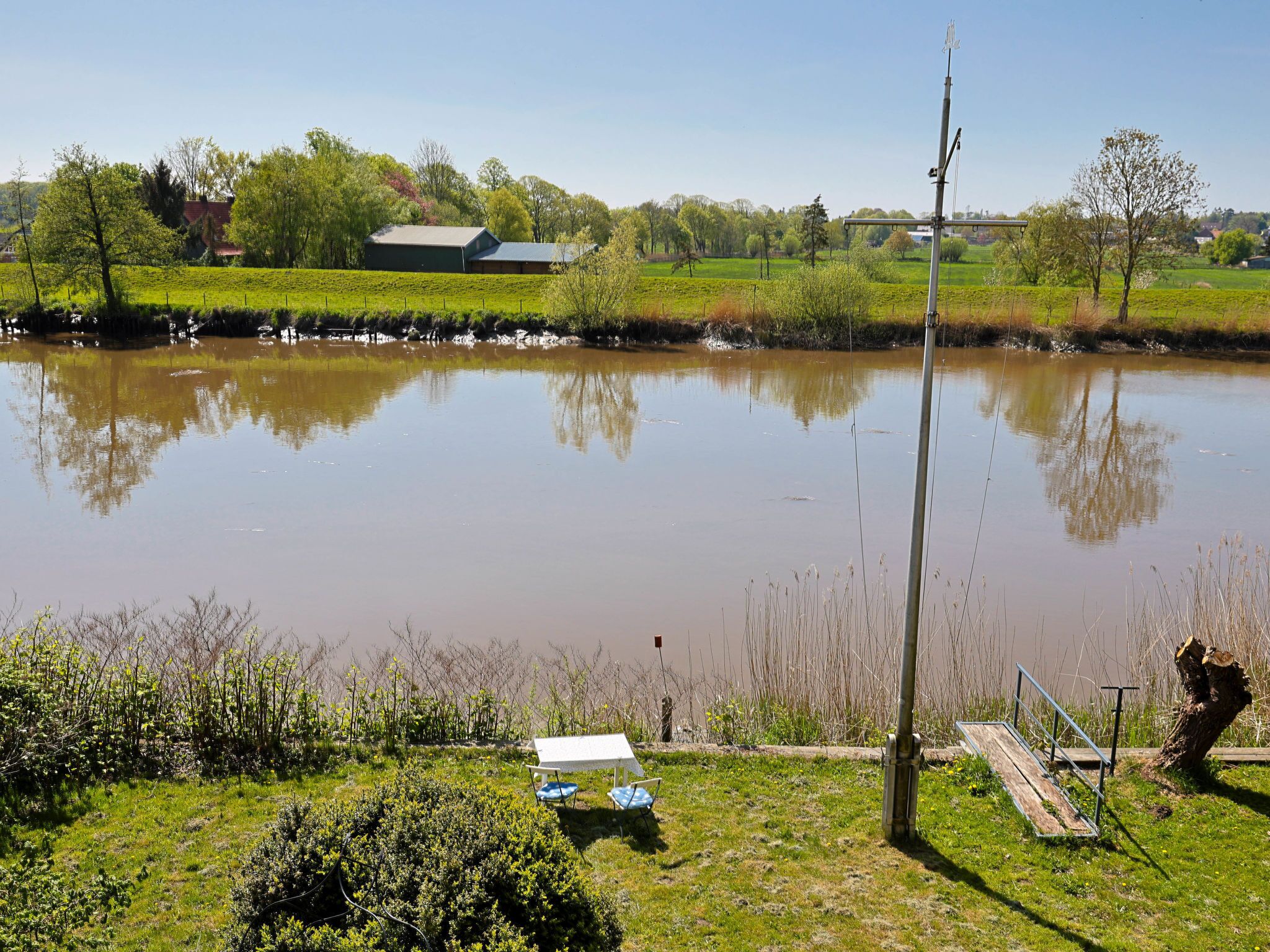 A calm lake with a dock and a table with chairs on the shore.