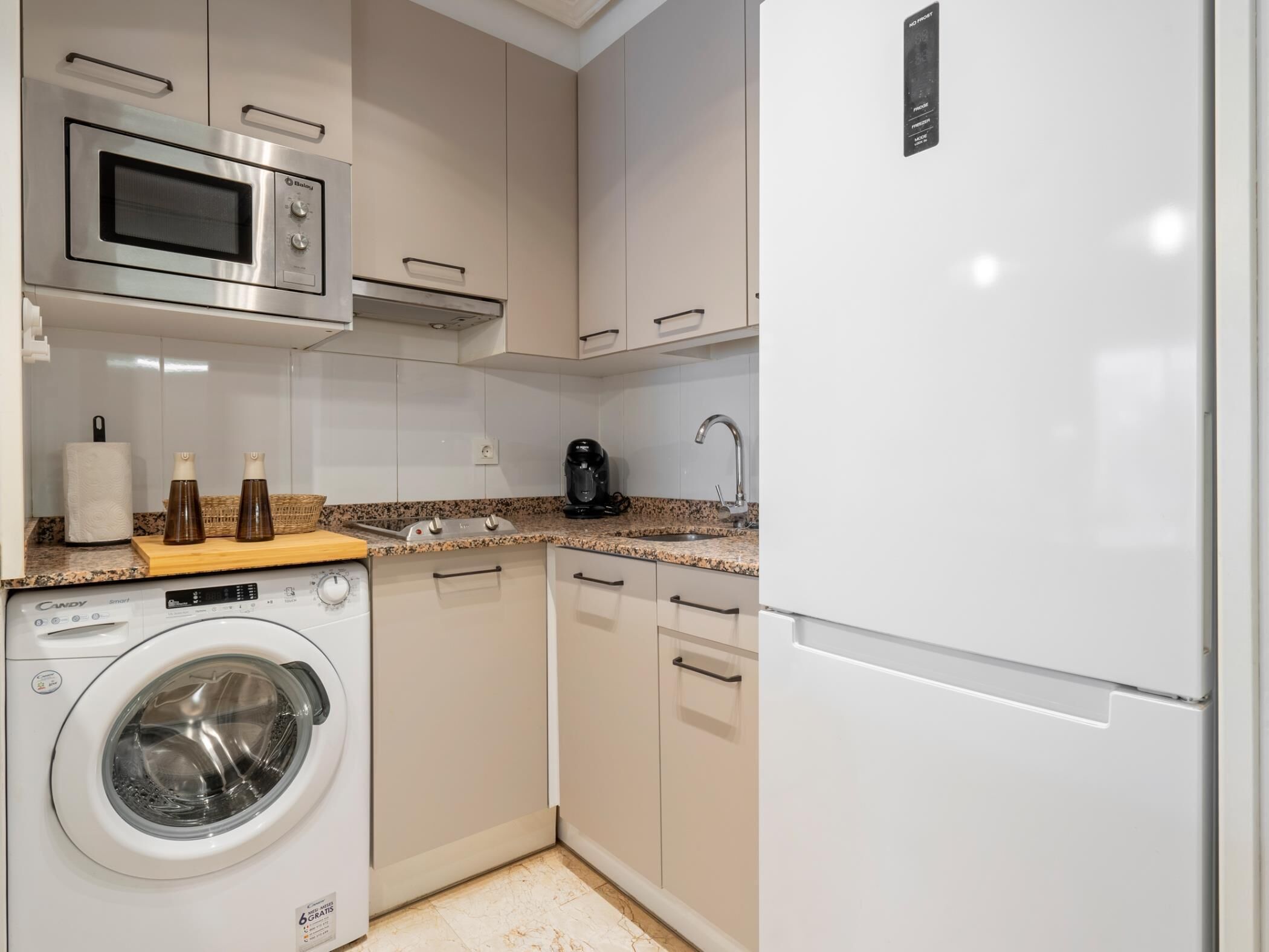 Une cuisine compacte équipée d’un lave-linge, d’un four à micro-ondes, d’une machine à café et d’un réfrigérateur.
