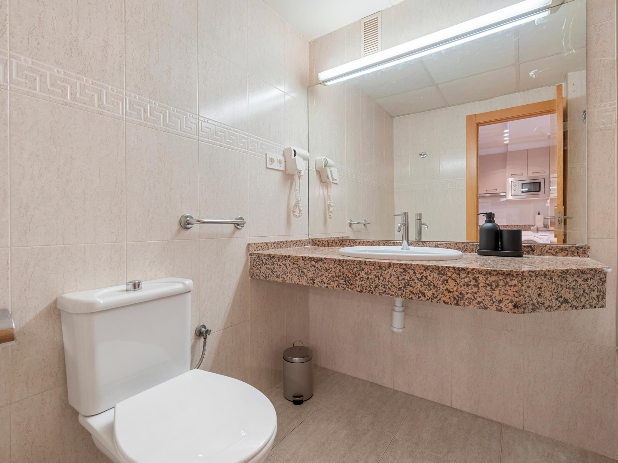 Un baño moderno con inodoro blanco, lavamanos de granito y un espejo grande.