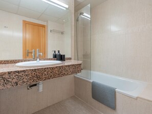 Une salle de bain moderne avec un lavabo surmonté d’un plan de travail en granit, une douche à parois de verre et une baignoire.