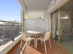 Un balcon avec une table ronde et quatre chaises, une porte vitrée et une vue sur des immeubles et des arbres.