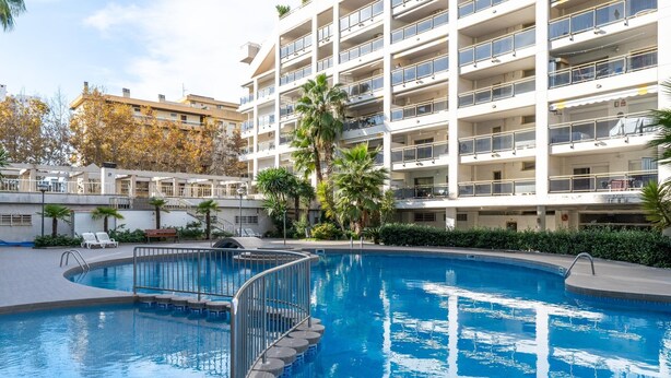 Une piscine au design incurvé, entourée d’un immeuble à plusieurs étages doté de balcons.