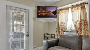 Una sala de estar con un televisor de pantalla plana montado en la pared, un sofá gris, una mesita y una ventana con cortinas estampadas.