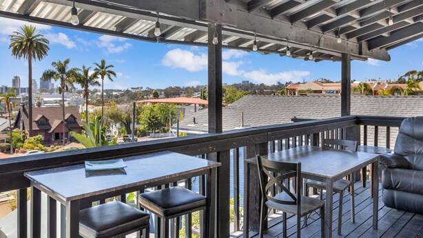 Una terraza techada al aire libre con una mesa y sillas, con vistas a una zona residencial con palmeras y casas.