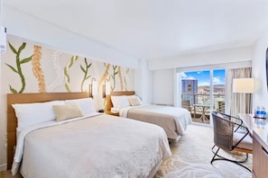 Quarto de hotel com duas camas, varanda e vista, e uma mesa com cadeira.