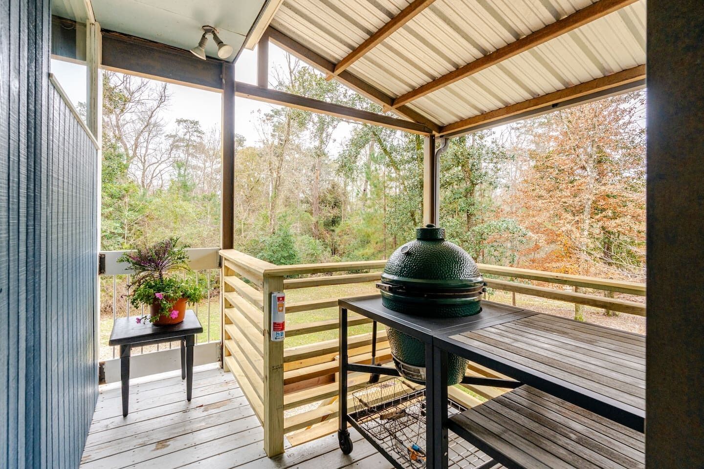 A covered outdoor deck with a grill, a small table with a potted plant, and a railing.
