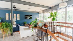 A spacious living area with a blue wall, wooden furniture, and large windows.