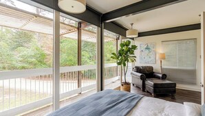 A bedroom with a large window, a bed, a leather sofa, and a potted plant.