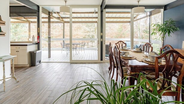 A spacious dining area with a wooden table and chairs, large windows, and a view of the outdoors.