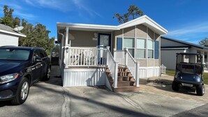 Une maison mobile de plain-pied, dotée d’une véranda, d’un petit escalier et d’une antenne parabolique.