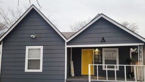 A two-story house with a dark gray exterior, a yellow front door, and a small porch with a white railing. - The Charming Vermont House. (Tulsa)