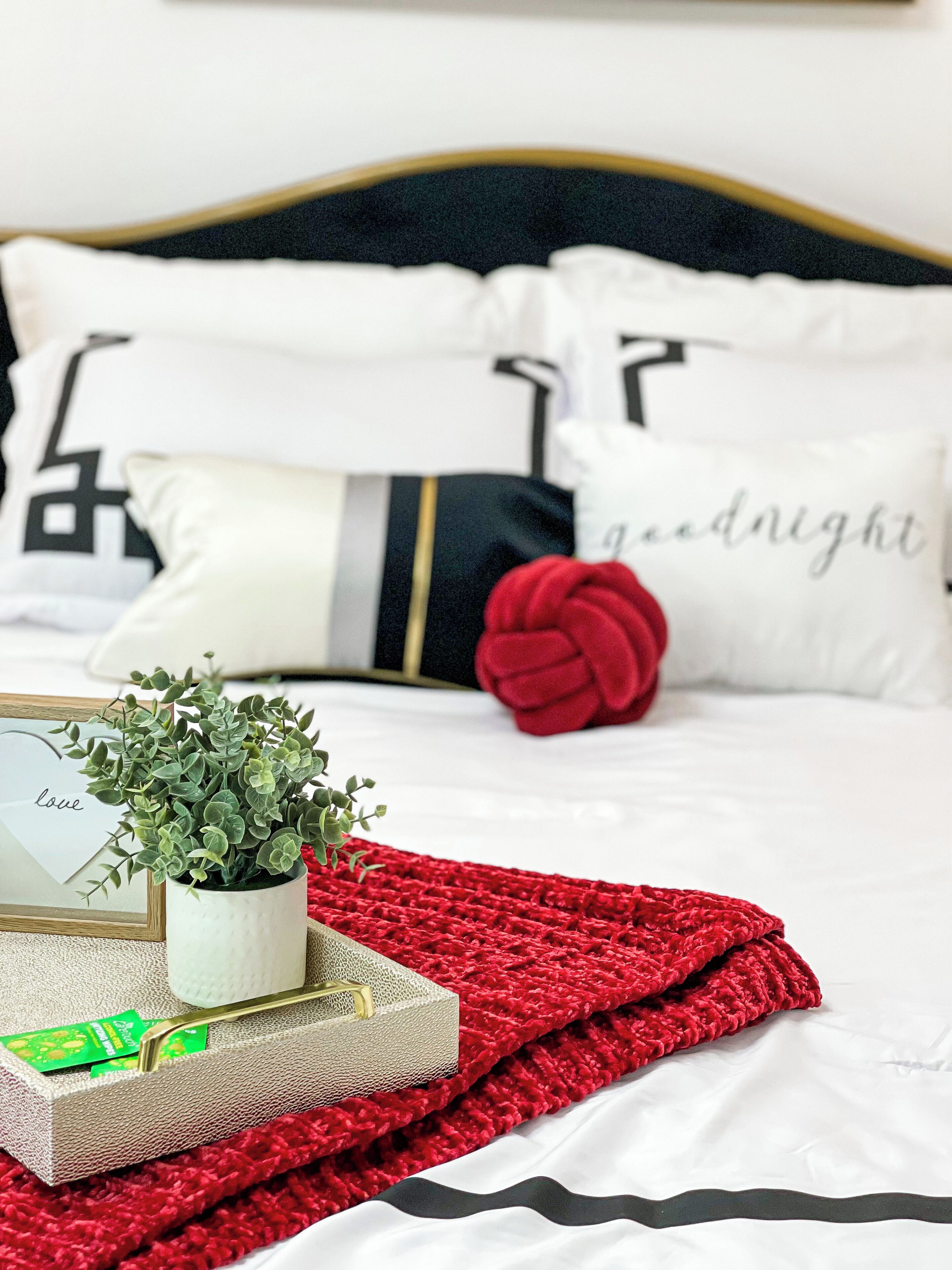 A neatly made bed with white and black bedding, a red knitted blanket, and decorative pillows with text.