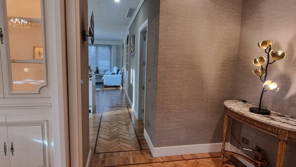 Un pasillo con suelo de espiga, una consola decorativa con una lámpara y vistas a una sala de estar con sofá y mesa de comedor.