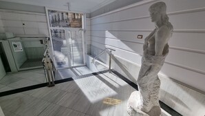 Une statue de marbre se trouve dans un couloir, devant une grille en métal et sur un sol carrelé.
